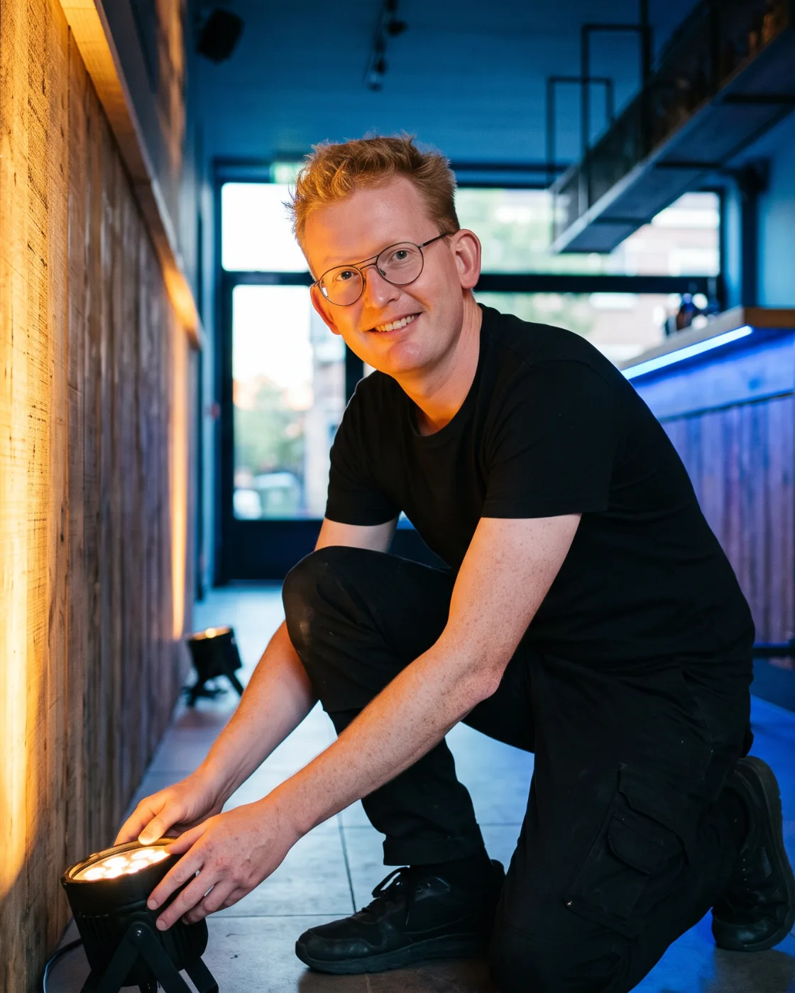 Mathieu Devlamynck plaatst een spot tegen een houten wand in een bar