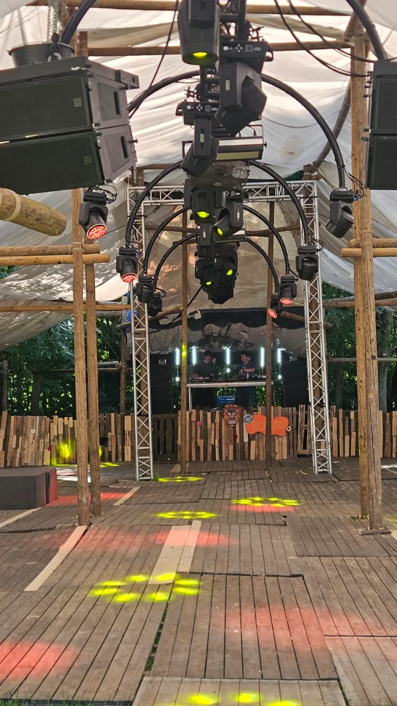 Houten festivalpodium met bogen van moving heads, line arrays en lichtvlekken op de dansvloer