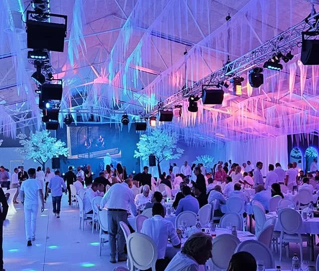 Witte feesttent met roze en blauw sfeerlicht boven gedekte tafels tijdens een trouwfeest
